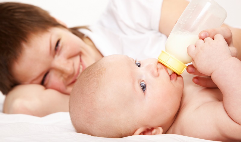Малыш пьет воду из бутылочки рядом с мамой